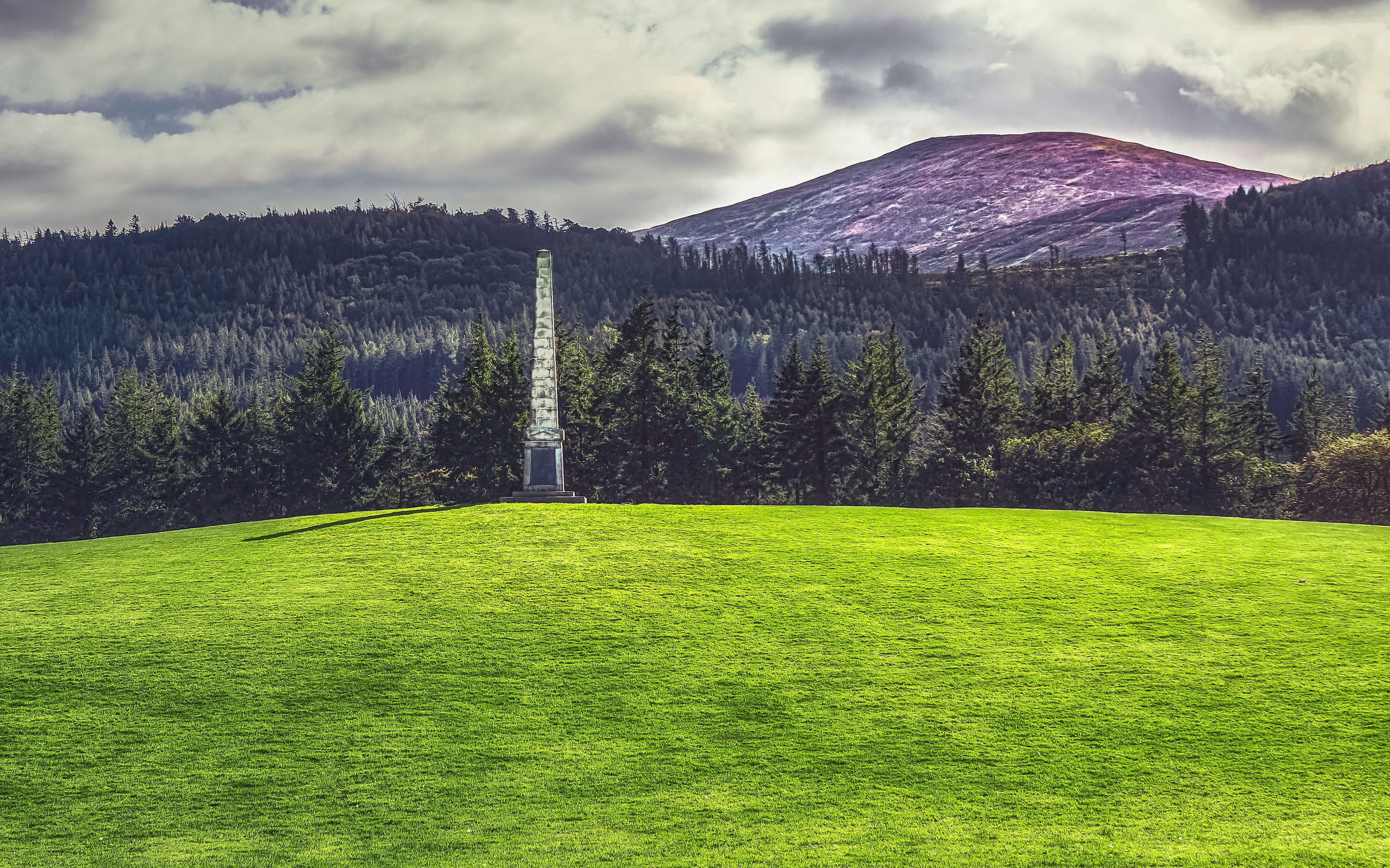 green grass field near green trees and mountain under cloudy sky during daytime